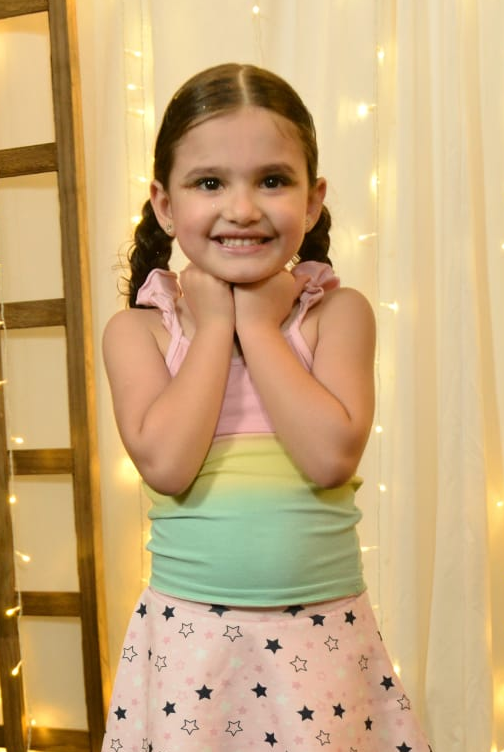 Lis Ayumi sorrindo, de tranças, com as mãos no queixo